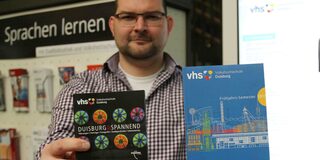 VHS-Mitarbeiter Hendrik Lange mit der Sonderbroschüre „Duisburg ist spannend“ und dem Gesamtprogramm für das Frühjahrssemester 2017