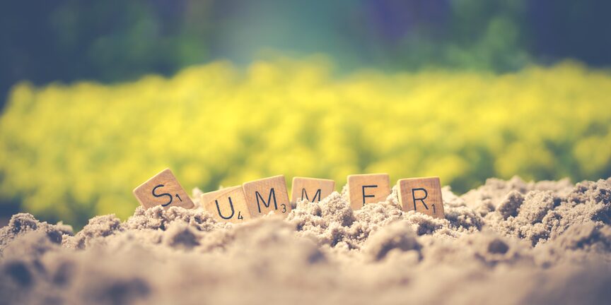 Scrabblesteine bilden das Wort "Summer" vor verschwommener sommerlicher Naturkulisse