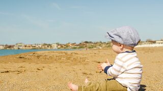 Ein Kind sitzt in der Sonne am Strand