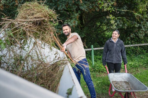 Zwei Teilnehmende am Social Day befüllen einen Container mit Grünschnitt und Unkraut