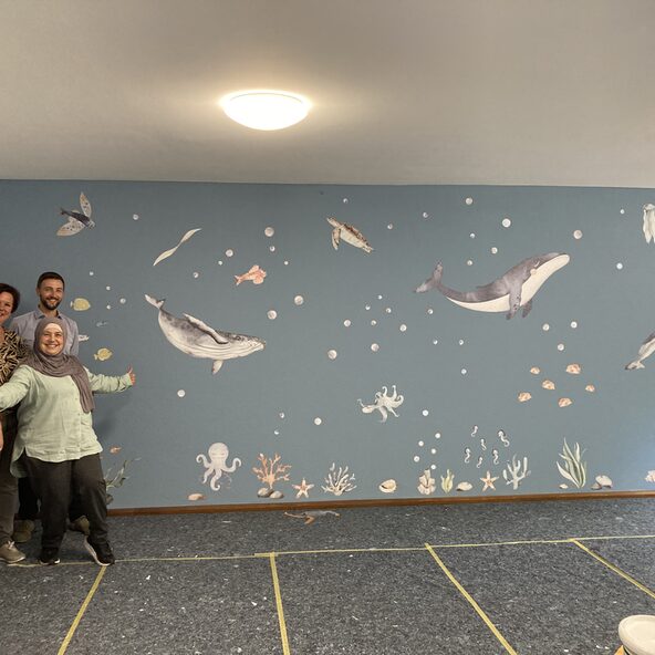Mitarbeitende von Aurelis und von HoHoHei vor der fertig gestalteten Wand