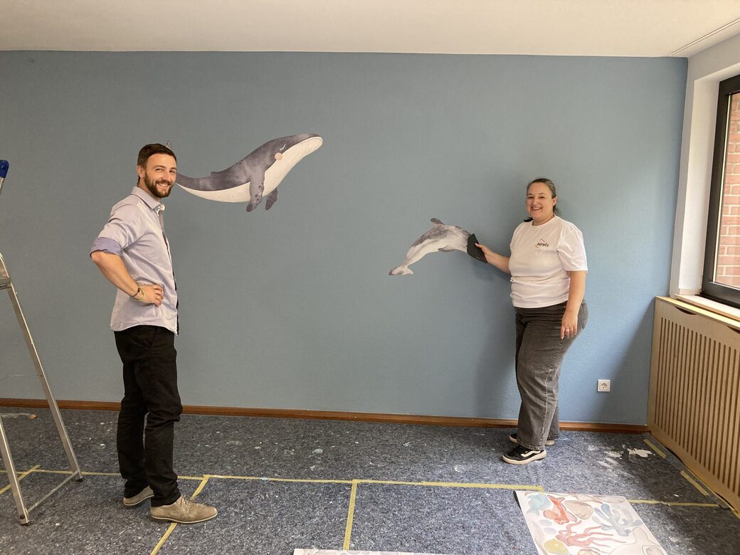 Zwei Mitarbeitende kleben Wale als Sticker auf die Wand.