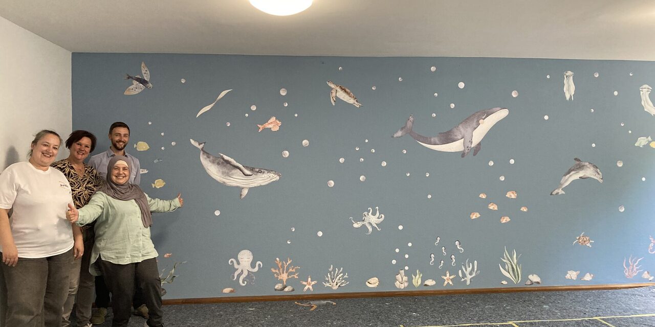 Mitarbeitende von Aurelis und von HoHoHei vor der fertig gestalteten Wand