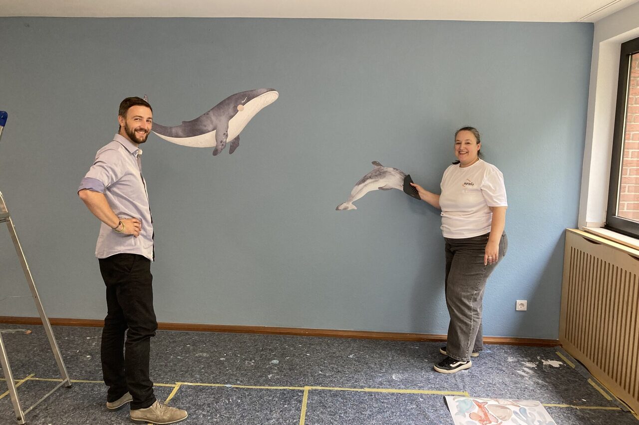 Zwei Mitarbeitende kleben Wale als Sticker auf die Wand.
