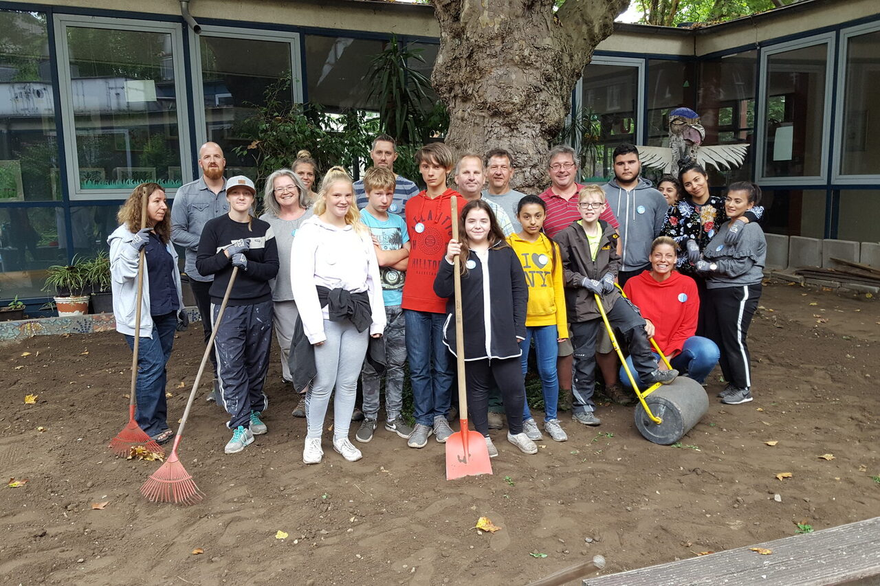 Eine Gruppe steht mit Arbeitsgeräten unter einem Baum.