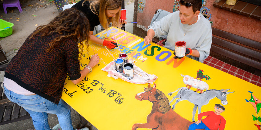 Drei Frauen malen ein neues Eingangsschild.