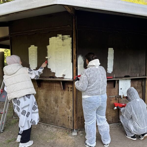 Mitarbeitende der Targo Bank streichen eine Hütte mit weißer Farbe an.