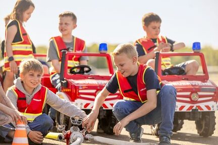 Kinder in Spielzeugfeuerwehrautos und mit einem Löschschlauch