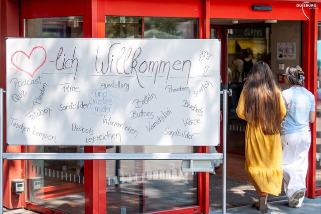 2 Personen betreten den Campus Marxloh. Auf einem Whiteboard stehen verschieden Angebote.