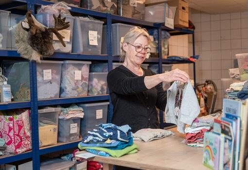 Frau sortiert Kleidung in der Babykleiderkammer
