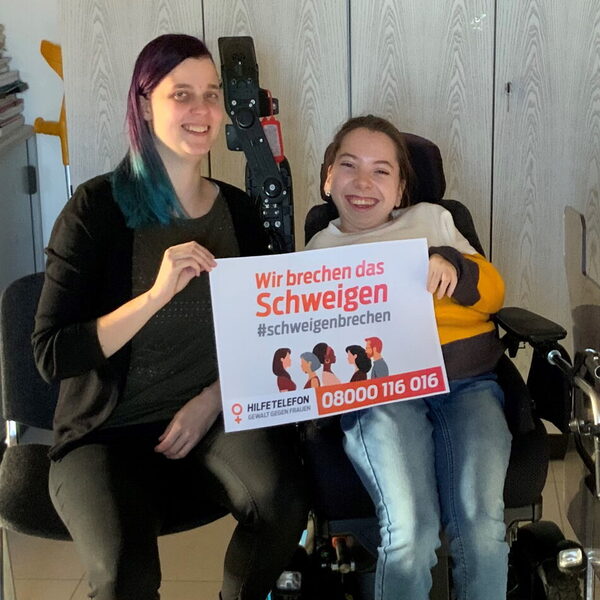 Zwei junge Frauen halten ein Schild mit der Aufschrift "wir brechen das Schweigen" in die Kamera