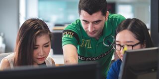 Ein Praktikant guckt seinen Kolleginnen über die Schulter