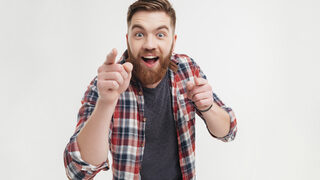 Excited bearded man in checkered shirt pointing fingers at camera