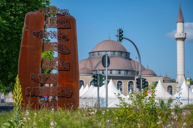 Rückseite der Dialogskulptur in Duisburg Marxloh als Teil des Marxloher Skulpturenwegs, mit der Moschee im Hintergrund.