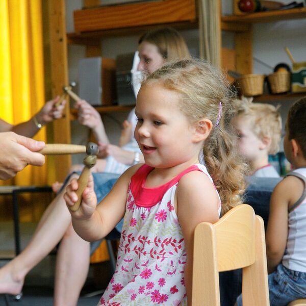 Mädchen auf Stuhl sitzend mit Klanghölzern
