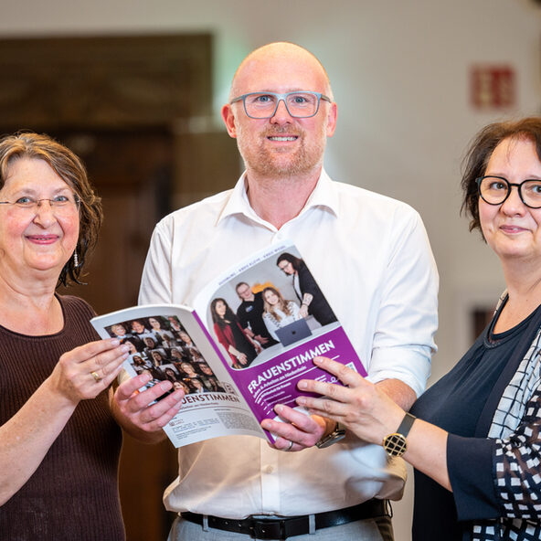 Drei Menschen halten ein Booklet in die Kamera