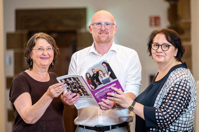 Drei Menschen halten eine Broschüre fest