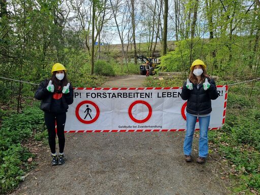 2 Mädchen stehen auf einem Waldweg, hinter Ihnen ein Banner "Stopp! Forstarbeiten! Lebensgefahr!
