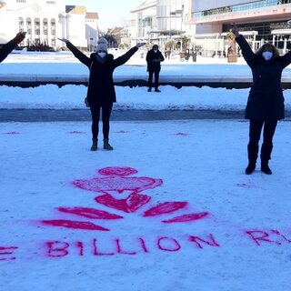 Die 3 Mitarbeiterinnen stehen mit Maske und erhobenen Armen hinter dem in den Schnee gesprühten LOGO von One Billion Rising