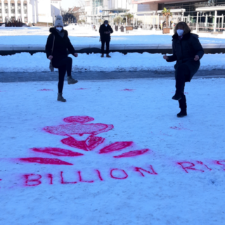 Die Mitarbeiterinnen stehen mit Maske und angezogenem linken Knie hinter dem in den Schnee gesprühten LOGO von One Billion Rising