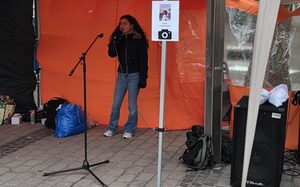 Eine junge Frau steht unter einen orangefarbenen Pavillon und singt in ein Mikrofon