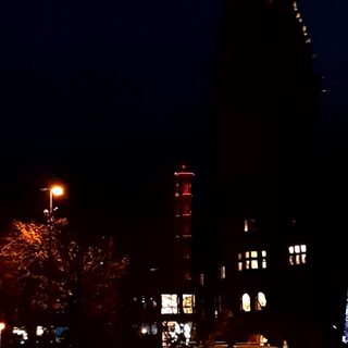 Der Stadtwerketurm leuchtet orange in der Dunkelheit, rechts daneben das Rathaus