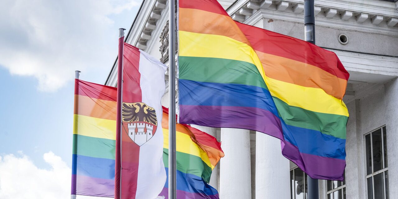 Zwei Regenbogenflaggen wehen zusammen mit der Flagge der Stadt Duisburg vor dem Theater