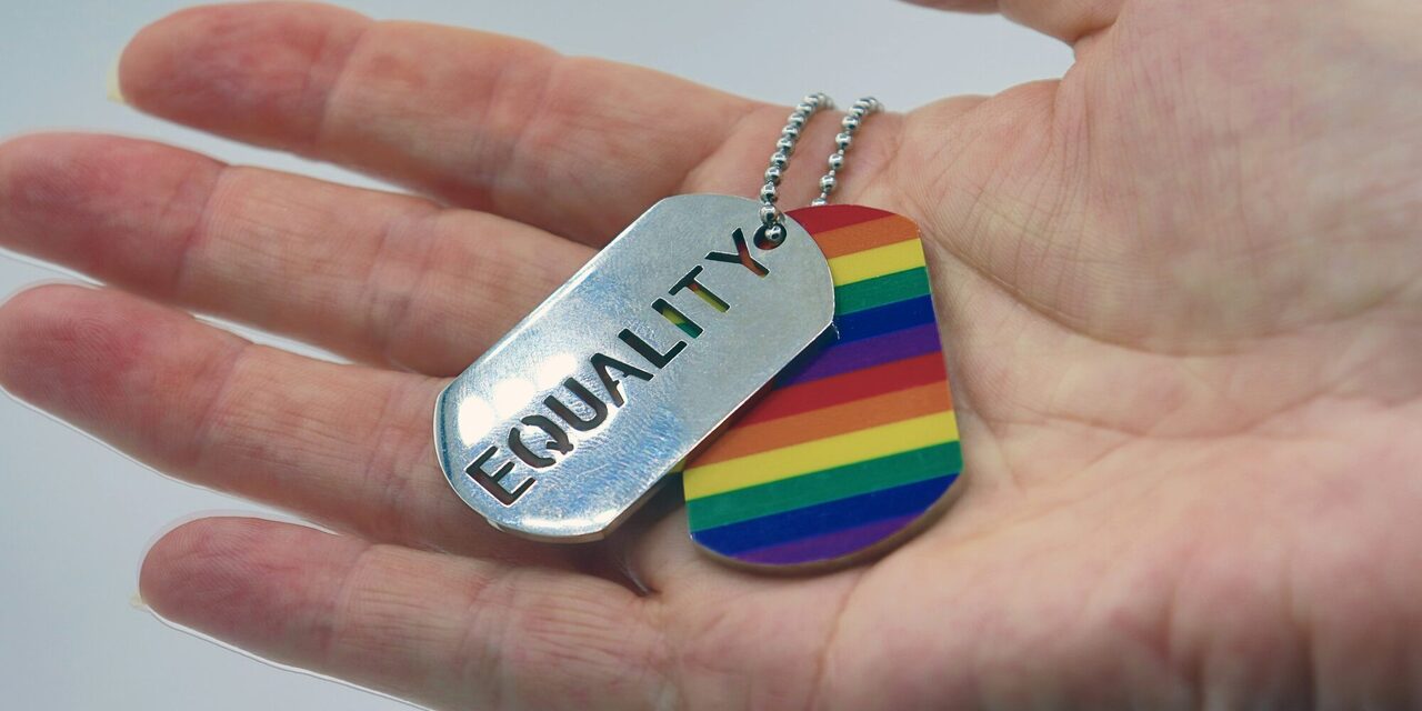 Kettenanhänger mit Equality und Regenbogenfarben in einer Hand