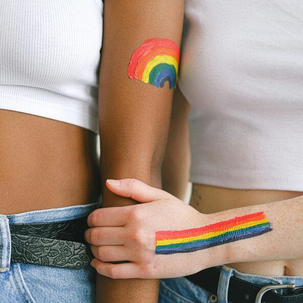 Ein mit Regenbogenflagge bemalter Arm hält einen anderen mit Regenbogen bemalten Arm fest