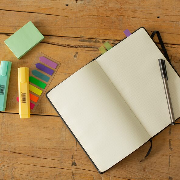 zwei Textmarker, ein Kugelschreiber und ein aufgeschlagenes, leeres Notizbuch