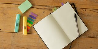 zwei Textmarker, ein Kugelschreiber und ein aufgeschlagenes, leeres Notizbuch