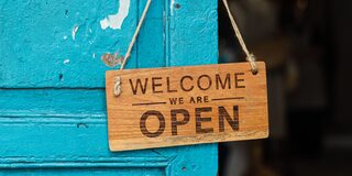 Blaue Tür mit Holzschild "Welcome we are open"