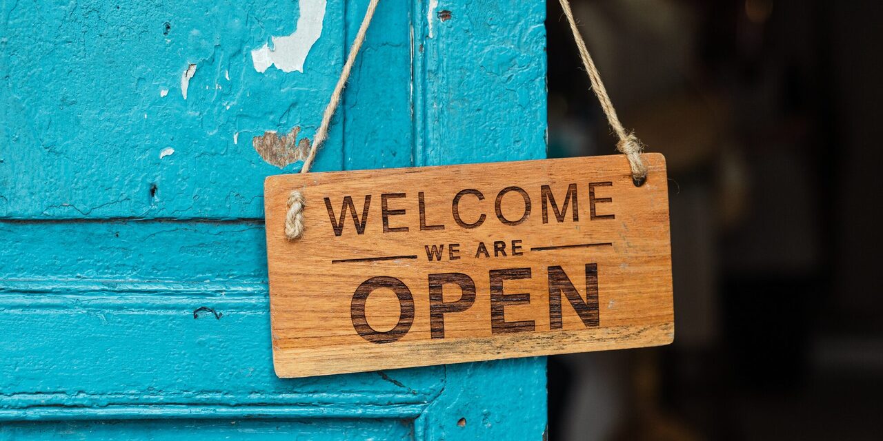 Blaue Tür mit Holzschild "Welcome we are open"