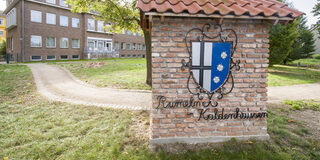 Rumel-Kaldenhausen: Wappen und ehemaliges Rathaus an der Kreuzung Rathausalle und Düsseldorfer Straße