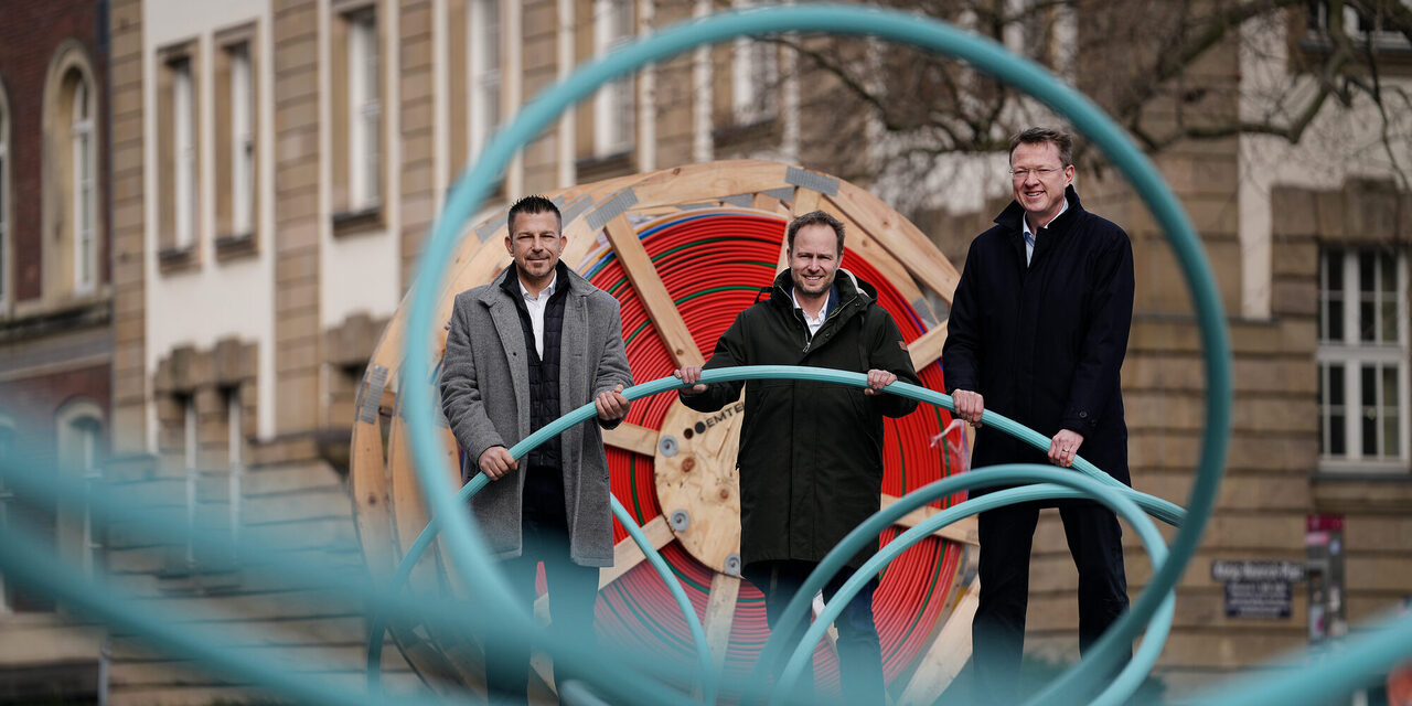 Drei Personen stehen vor einer großen Kabeltrommel und halten ein Glasfaserkabel fest.