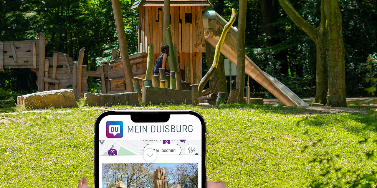 Im Hintergrund ist ein Spielplatz zu sehen, im Vordergrund ein Handy mit dem Spielplatzfinder
