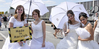 Frauen in Brautkleidern halten ein Made in Marxloh-Schild in den Händen
