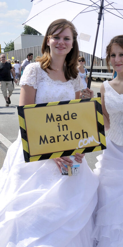 Frauen in Brautkleidern halten ein Made in Marxloh-Schild in den Händen